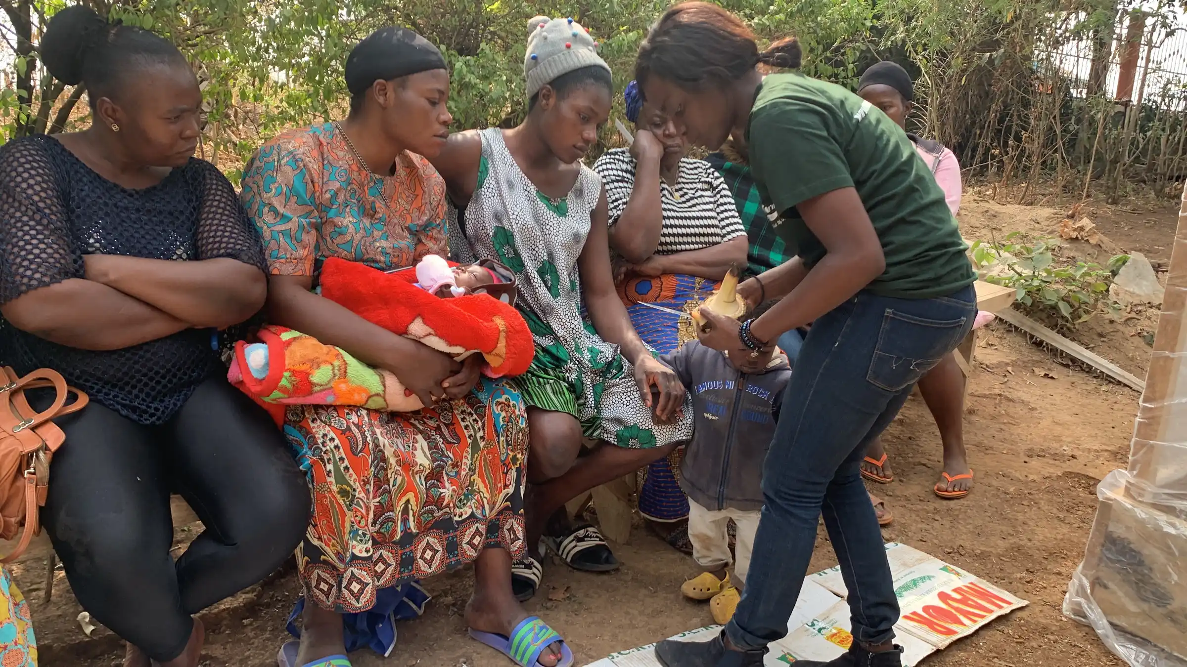 Women farmers sit together in a field while a Mumita staff member hands out materials