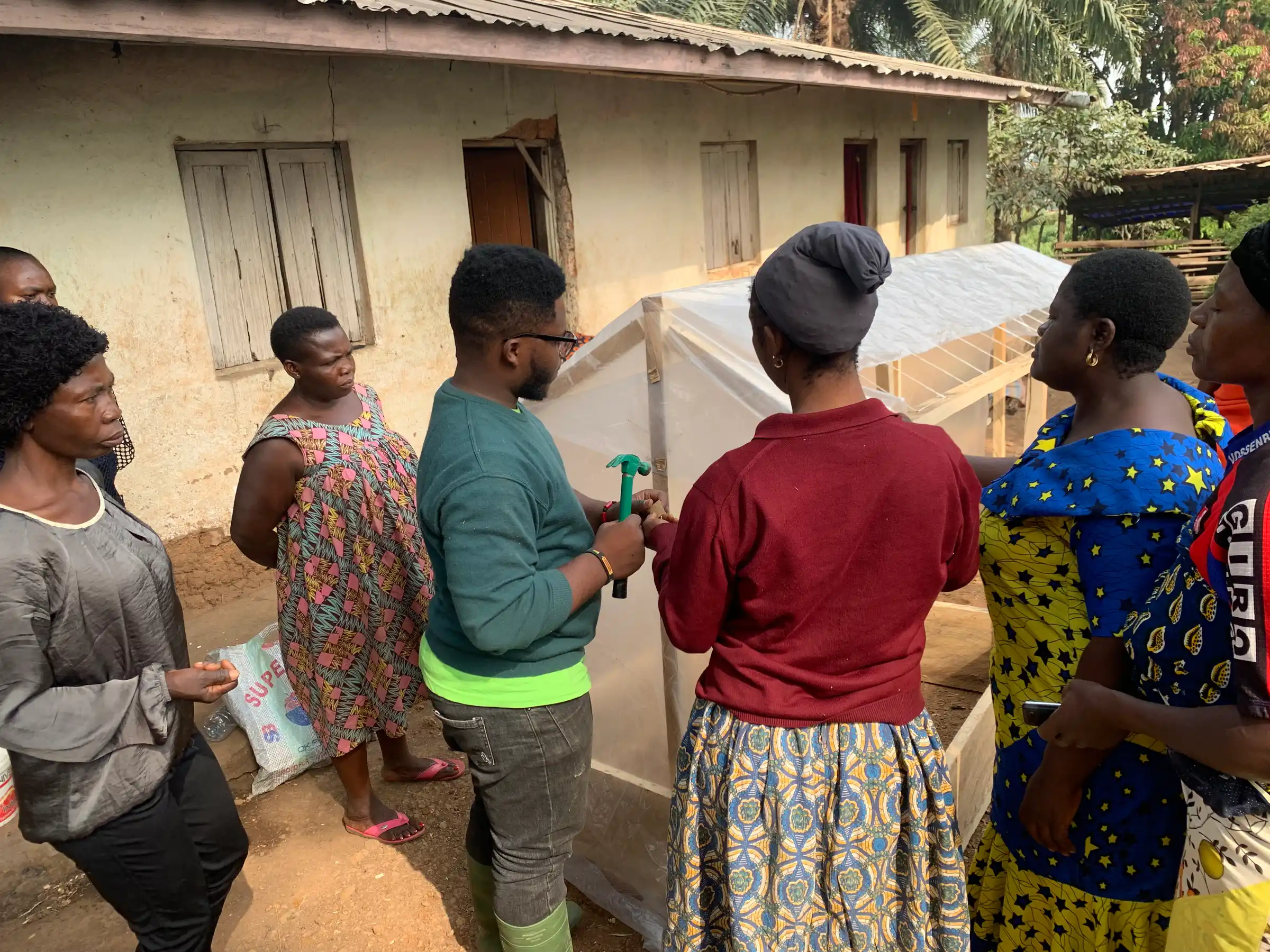 A Mumita trainer with women farmers beside the small greenhouse they have just covered in plastic