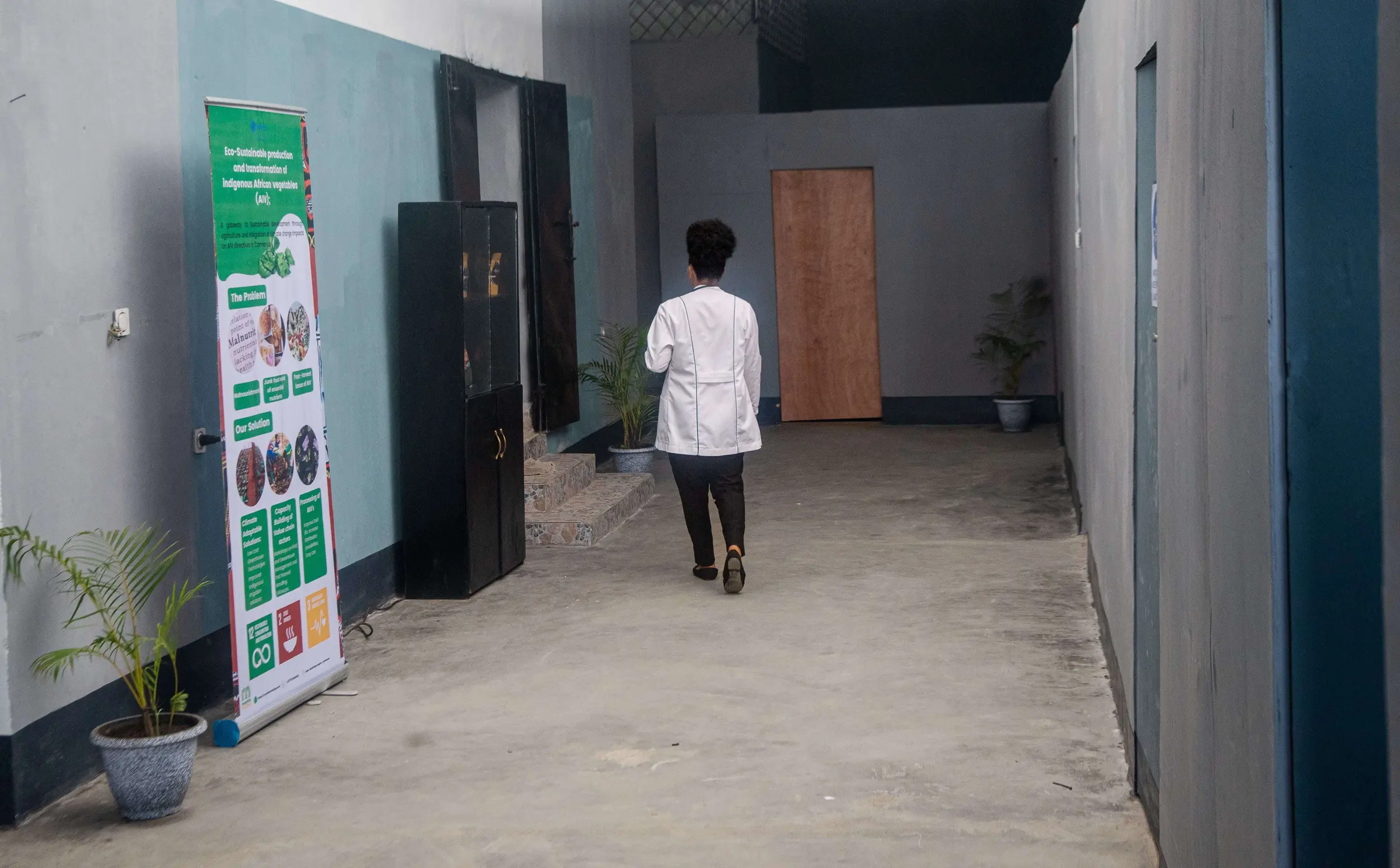 A staff member in a white coat walks down a corridor of the Bonduma Gate facility, past a pull-up banner