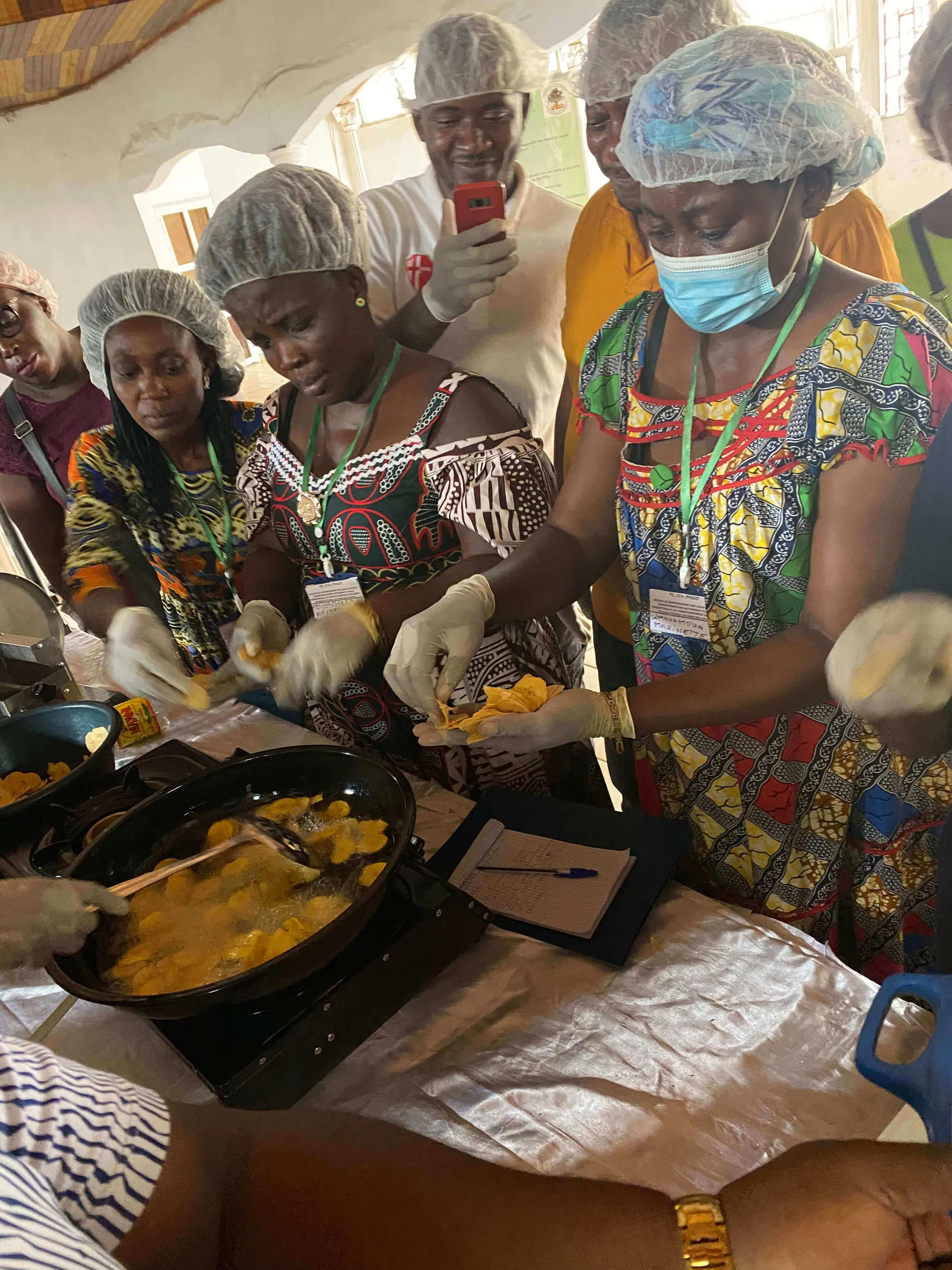 Women in hairnets and gloves frying and sorting plantain chips at a value-addition training
