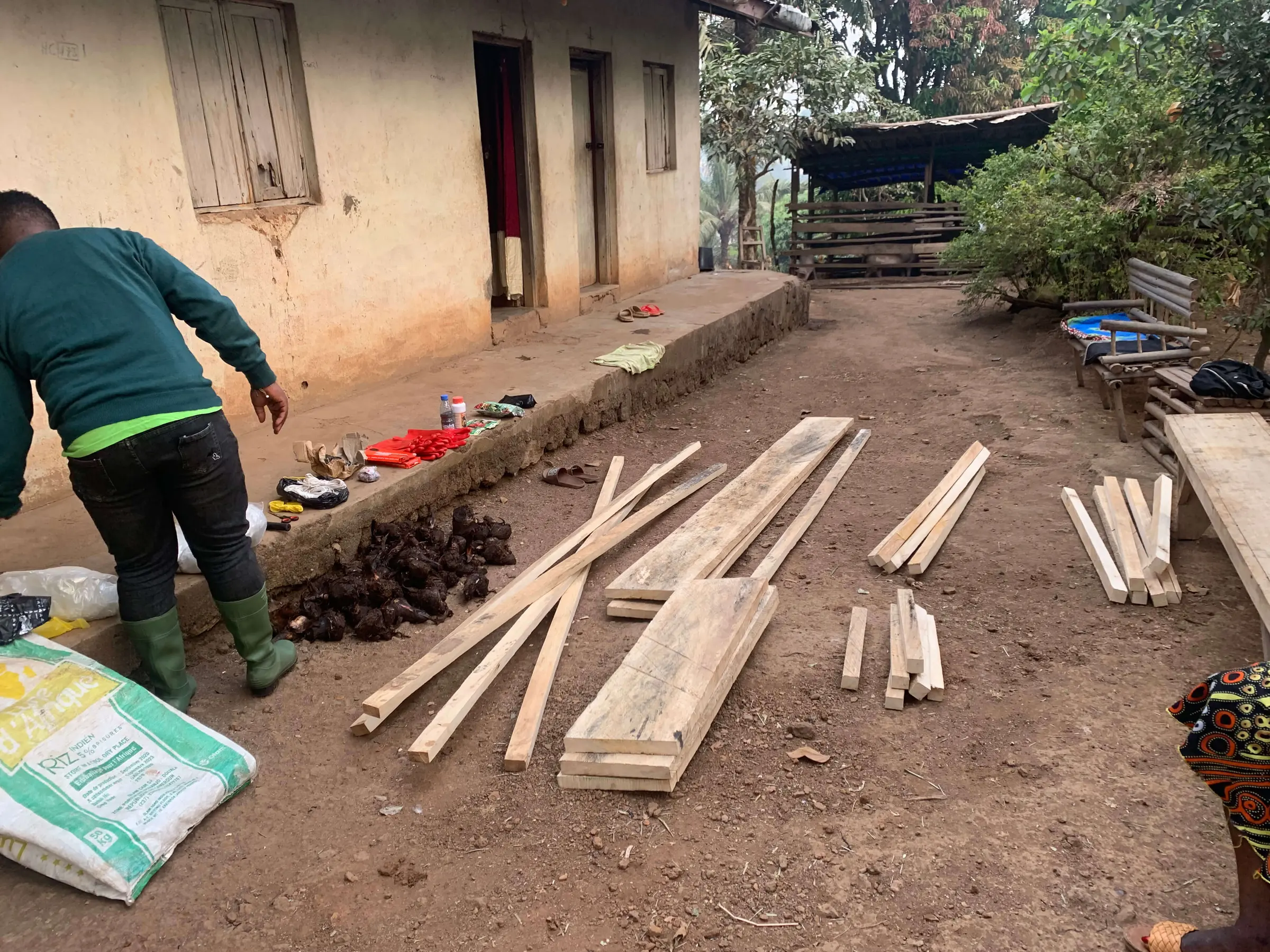 Timber, farm inputs and tools laid out in a village yard before a greenhouse build