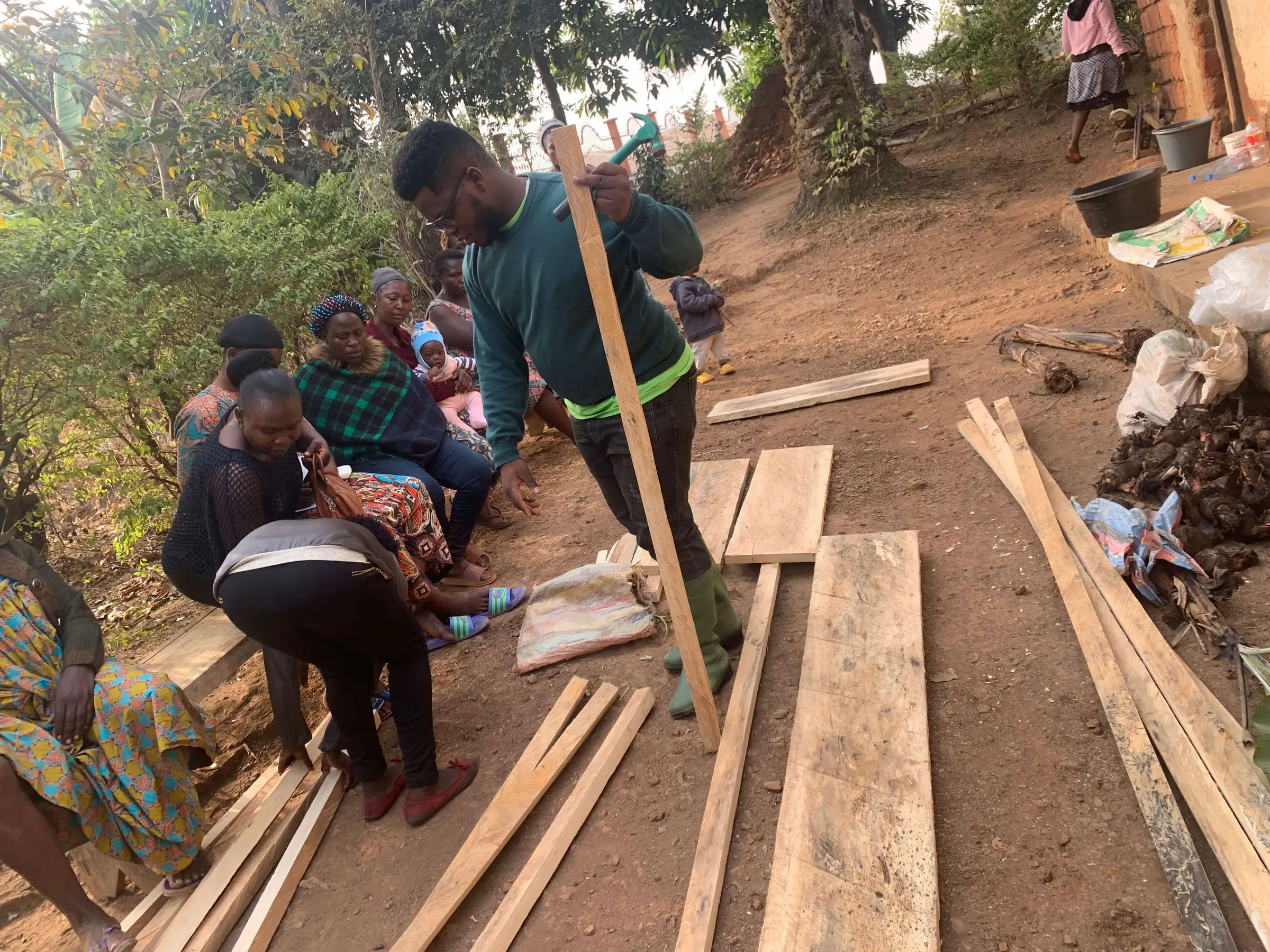 A Mumita trainer lifts a length of timber for a greenhouse frame while women farmers look on