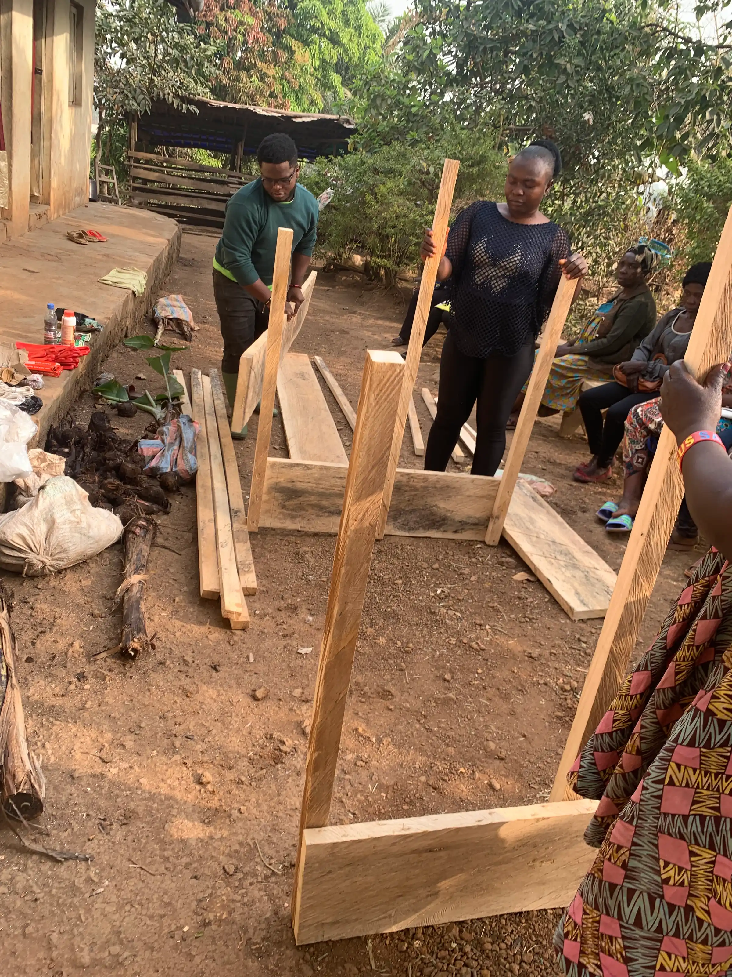 Women farmers and a Mumita trainer put up the first timber posts of a greenhouse frame in a village yard