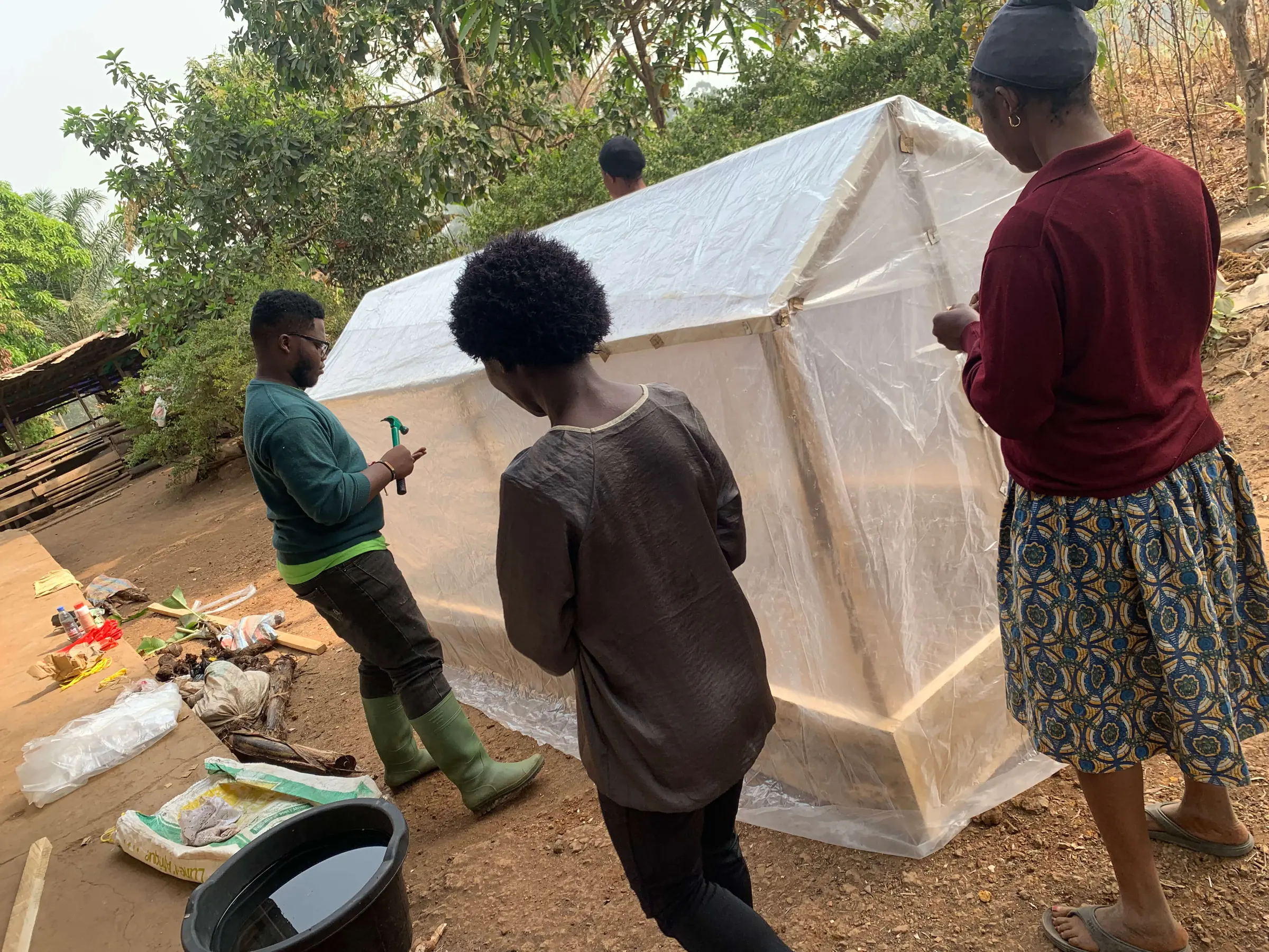 Community members and a Mumita trainer beside the finished greenhouse, covered in clear plastic