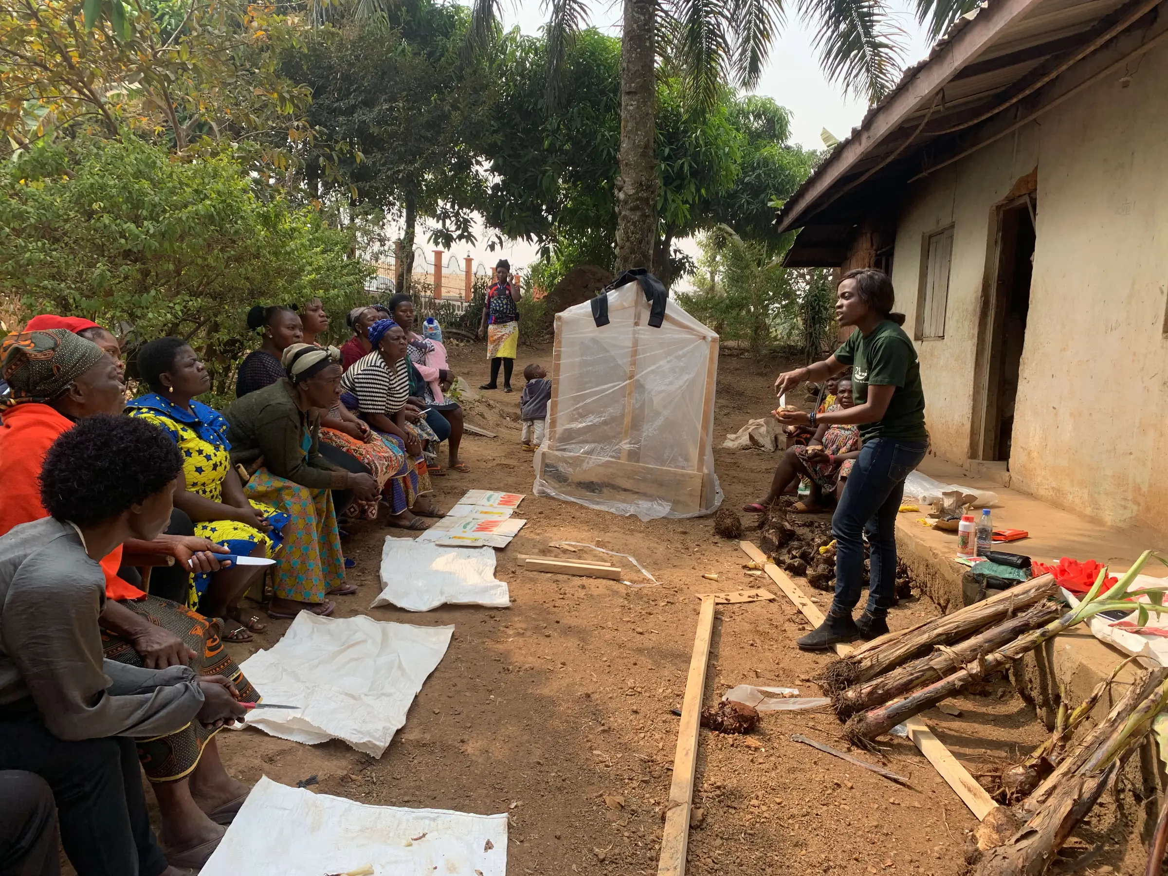 A trainer shows a group of seated farmers how to build a small greenhouse