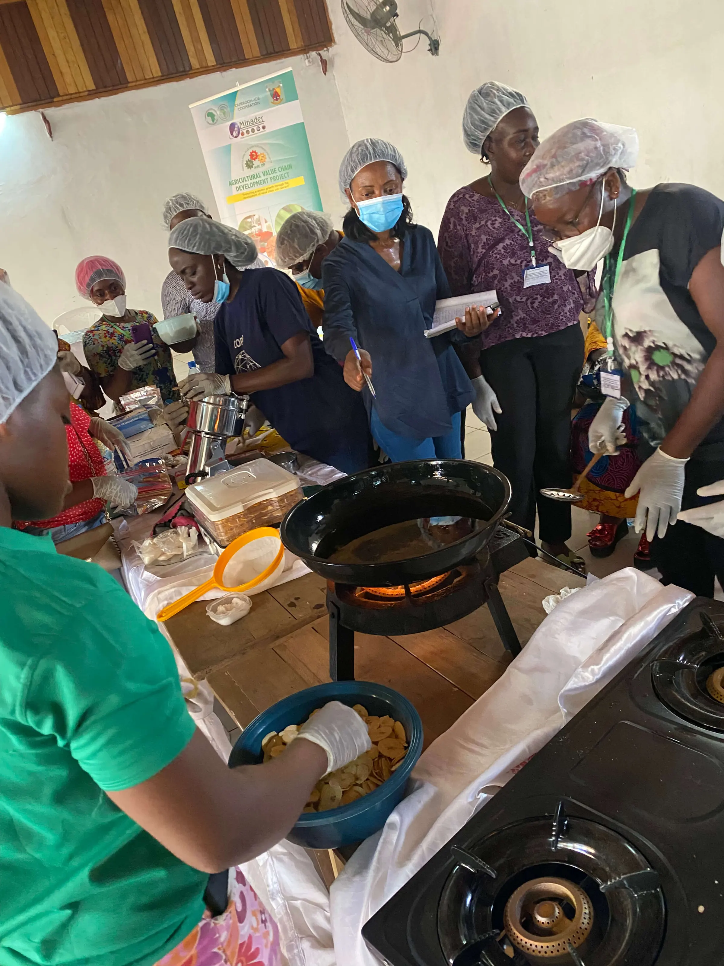 Trainees in hairnets cook together around a gas stove at a food processing session