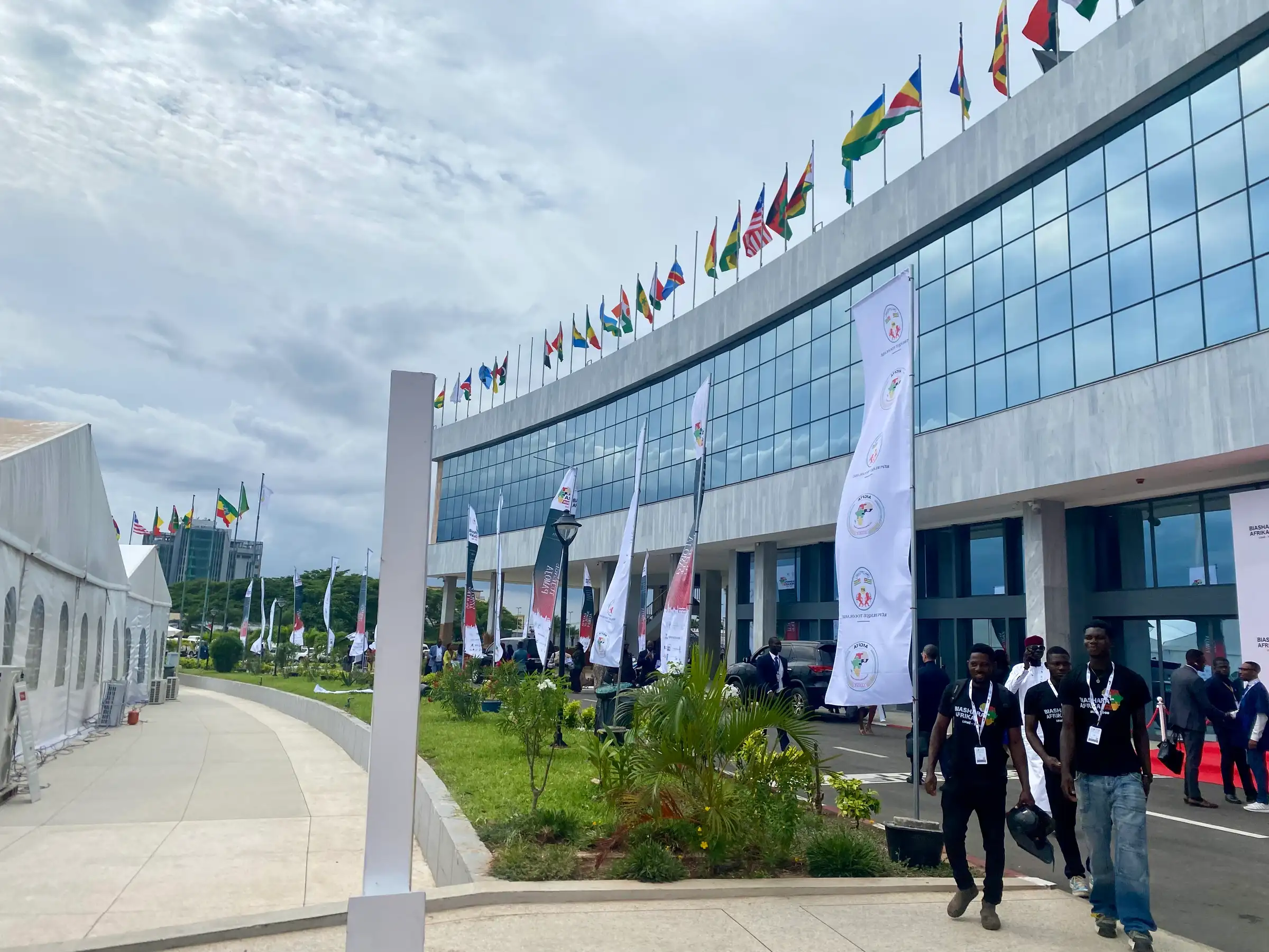 A row of national flags outside a conference venue, delegates walking in