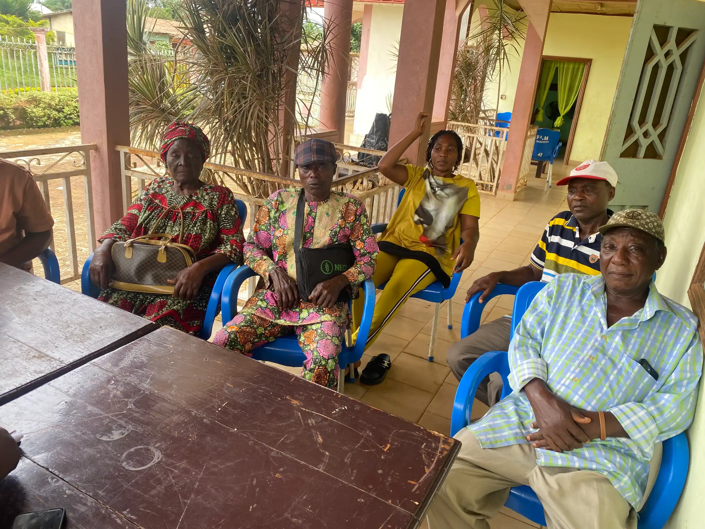 Older farmers seated in plastic chairs at a group meeting on a veranda