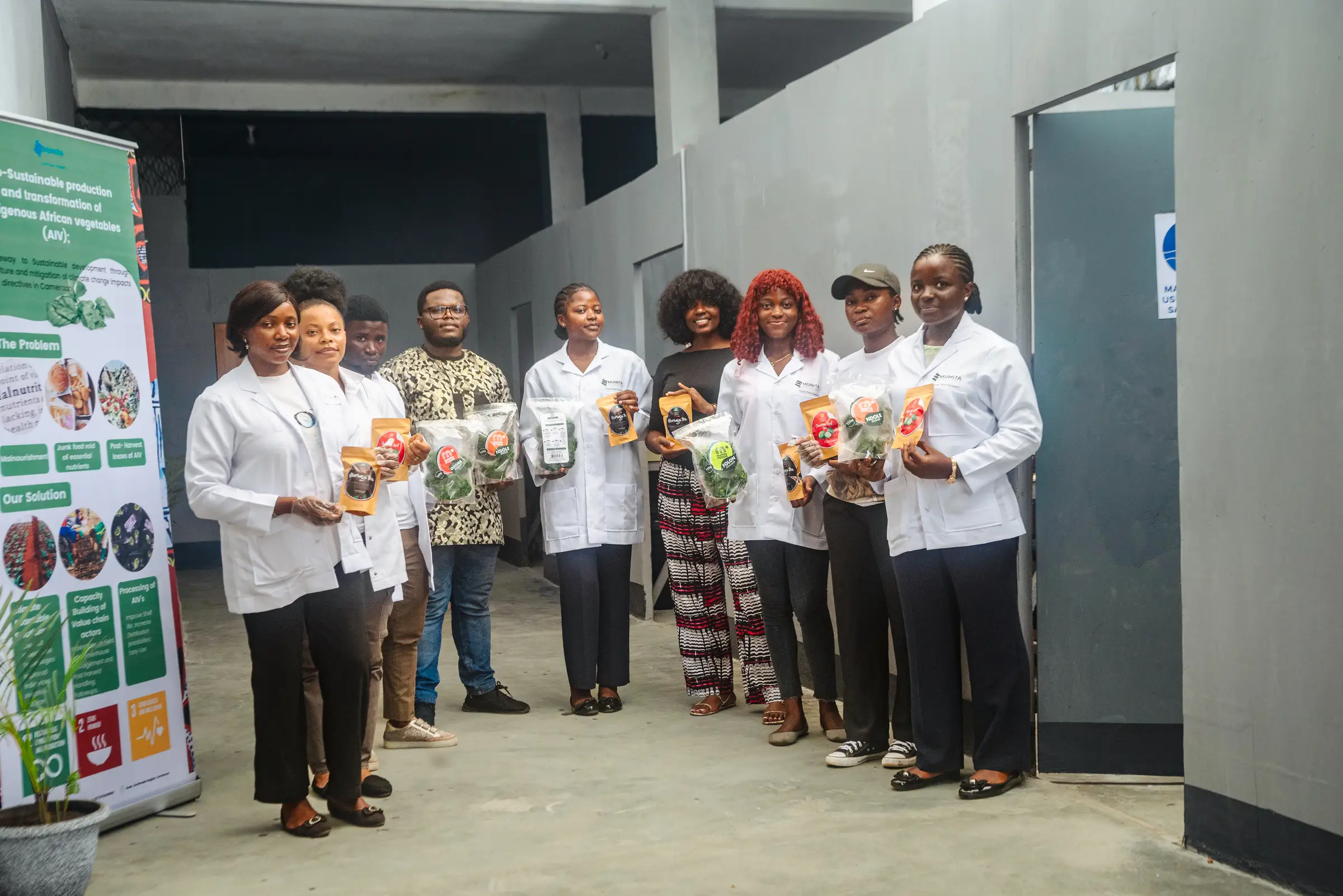 Mumita staff in white coats line the corridor of the Bonduma Gate facility beside a pull-up banner