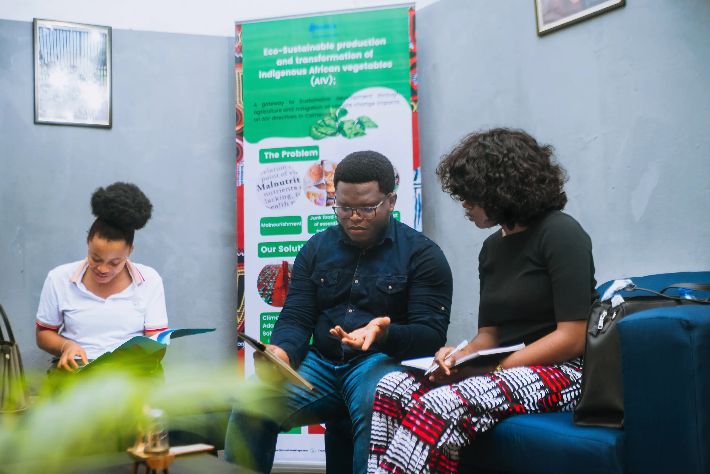 Three people on a sofa review documents beside a Mumita project banner