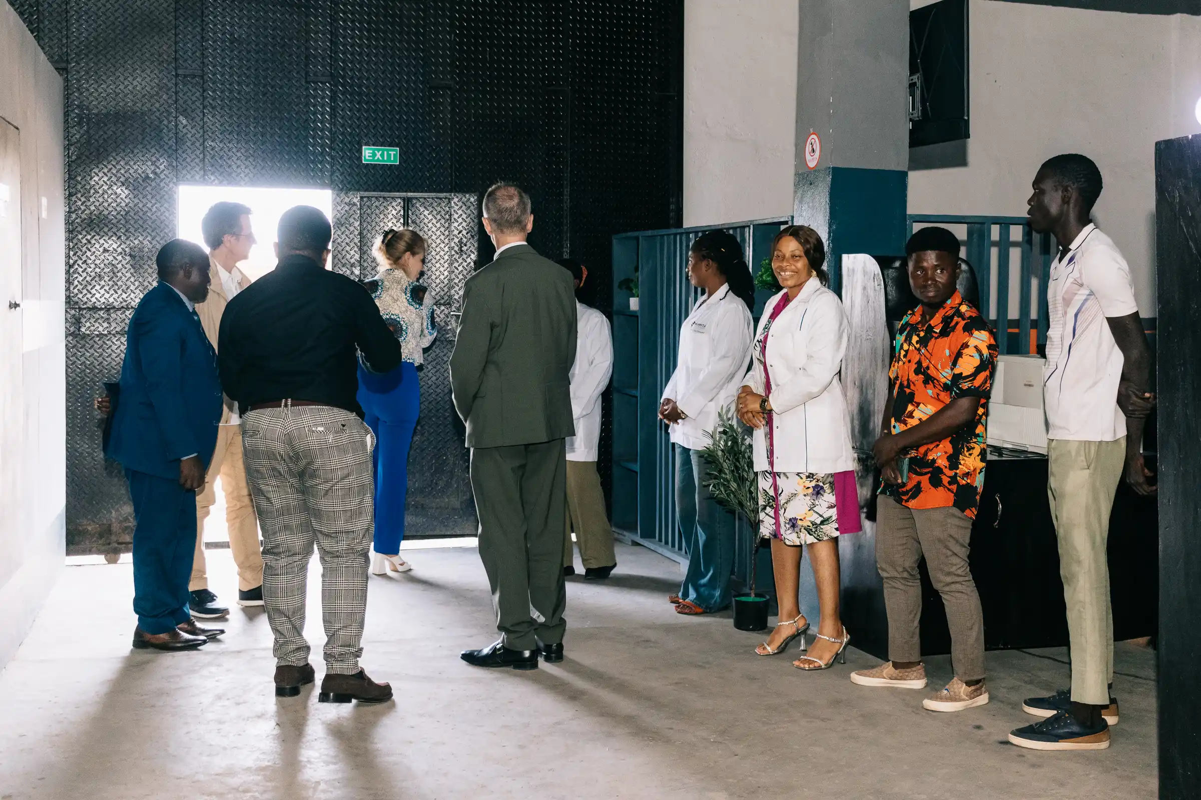 The Mumita team in white coats and visitors stand in a line outside the gate of the Bonduma Gate facility