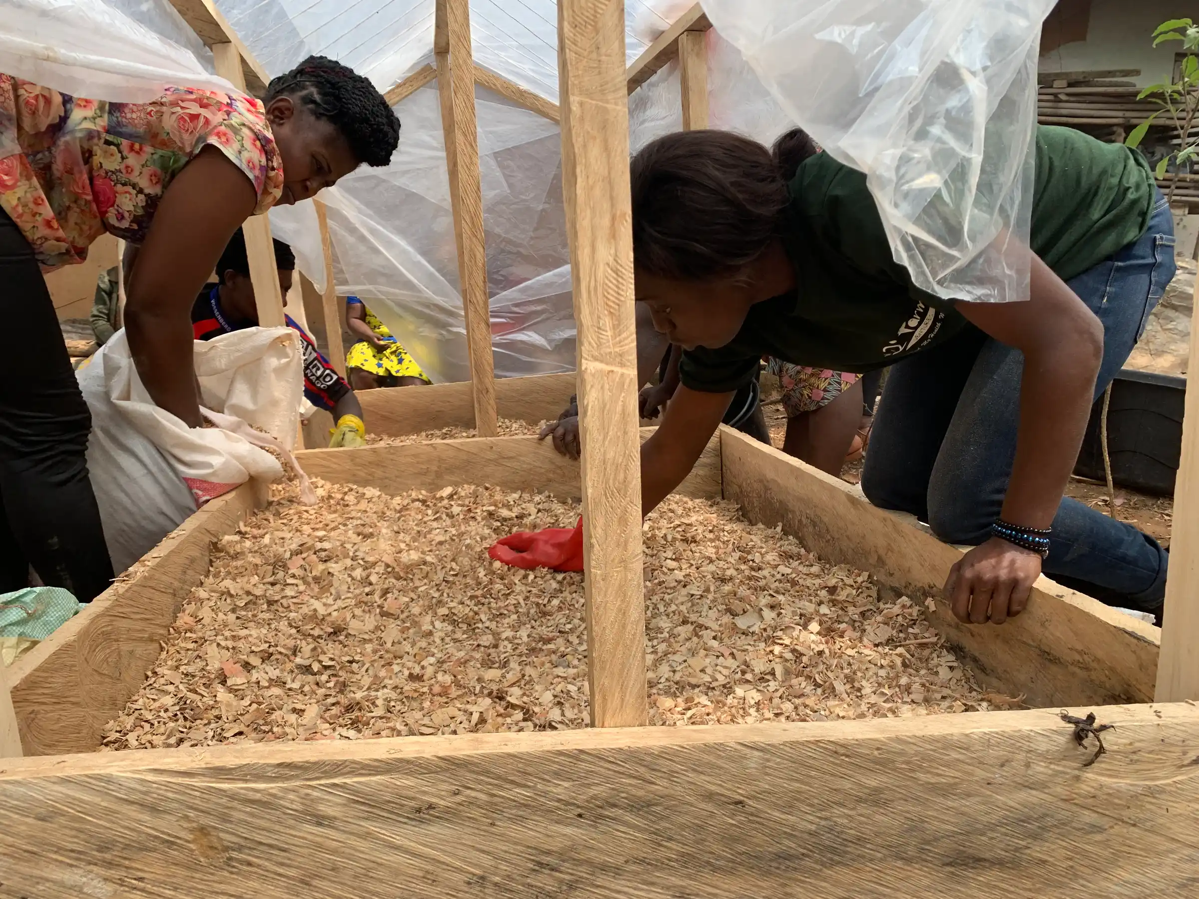 Women fill a timber raised bed with sawdust during a hands-on session