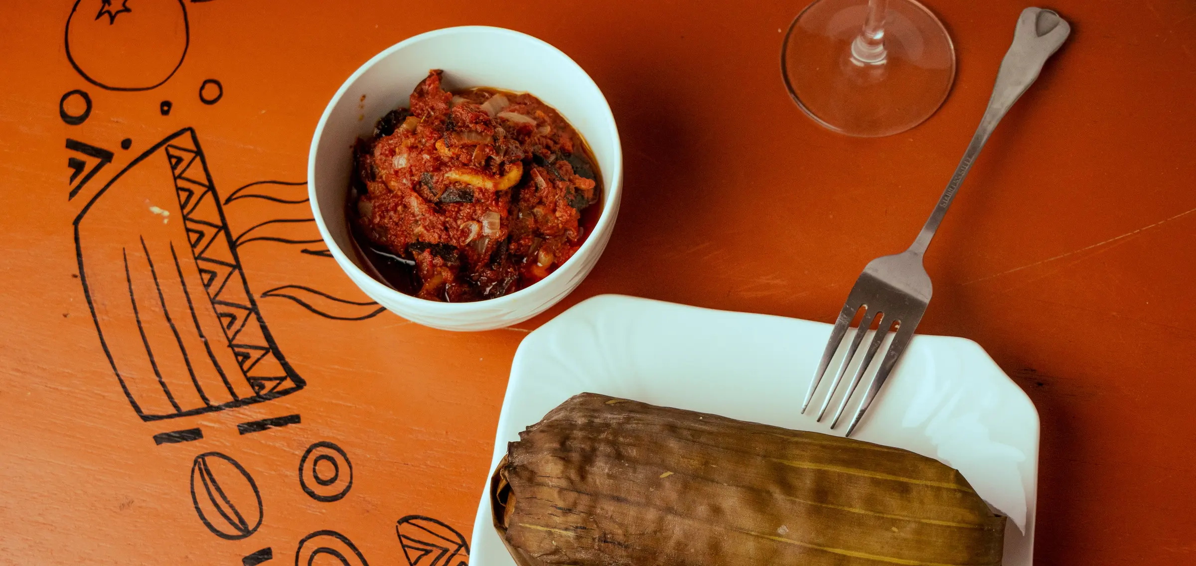 Leaf-wrapped dishes served with a bowl of red stew on a patterned table