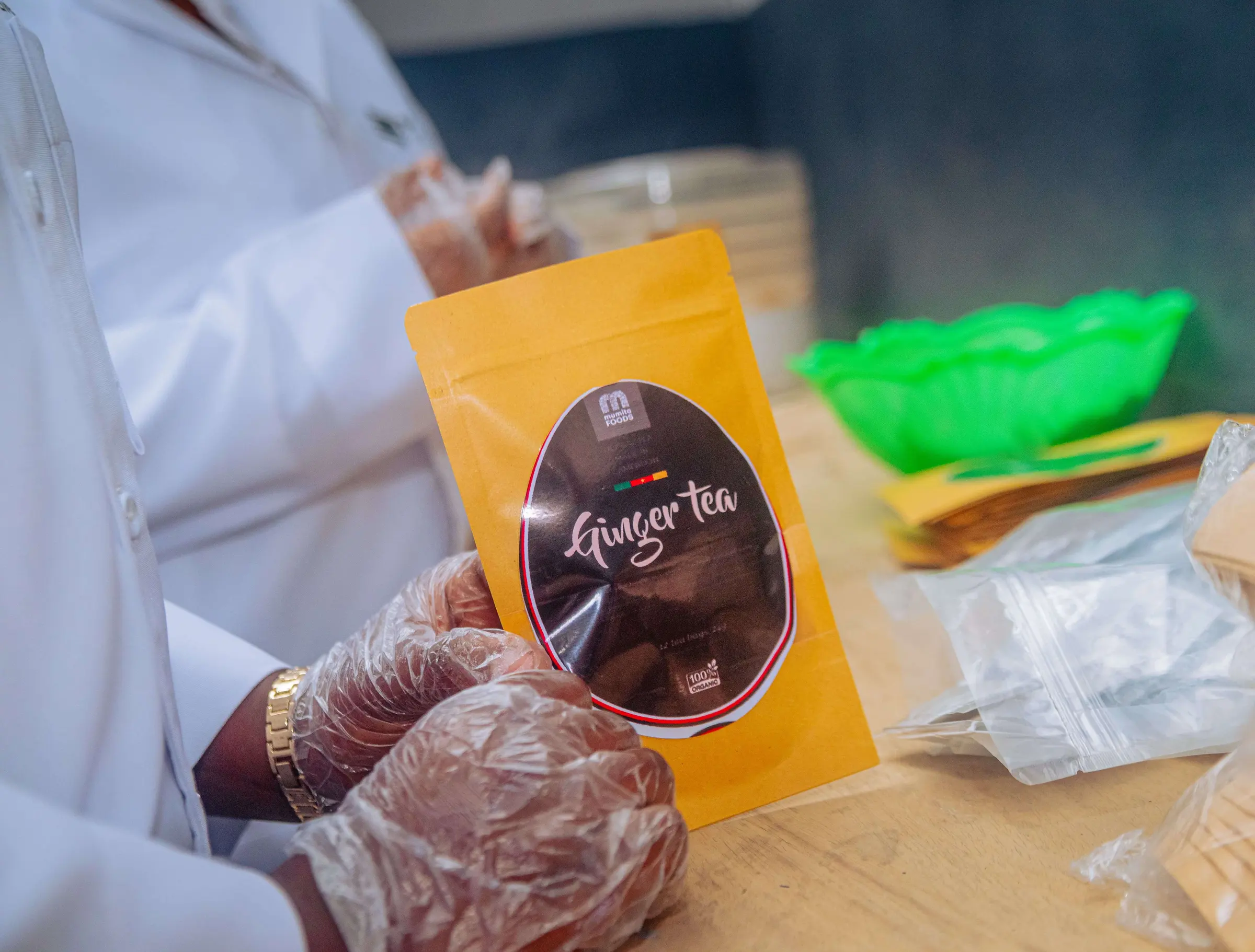 Gloved hands holding a pouch of Mumita Foods ginger tea at the packing bench