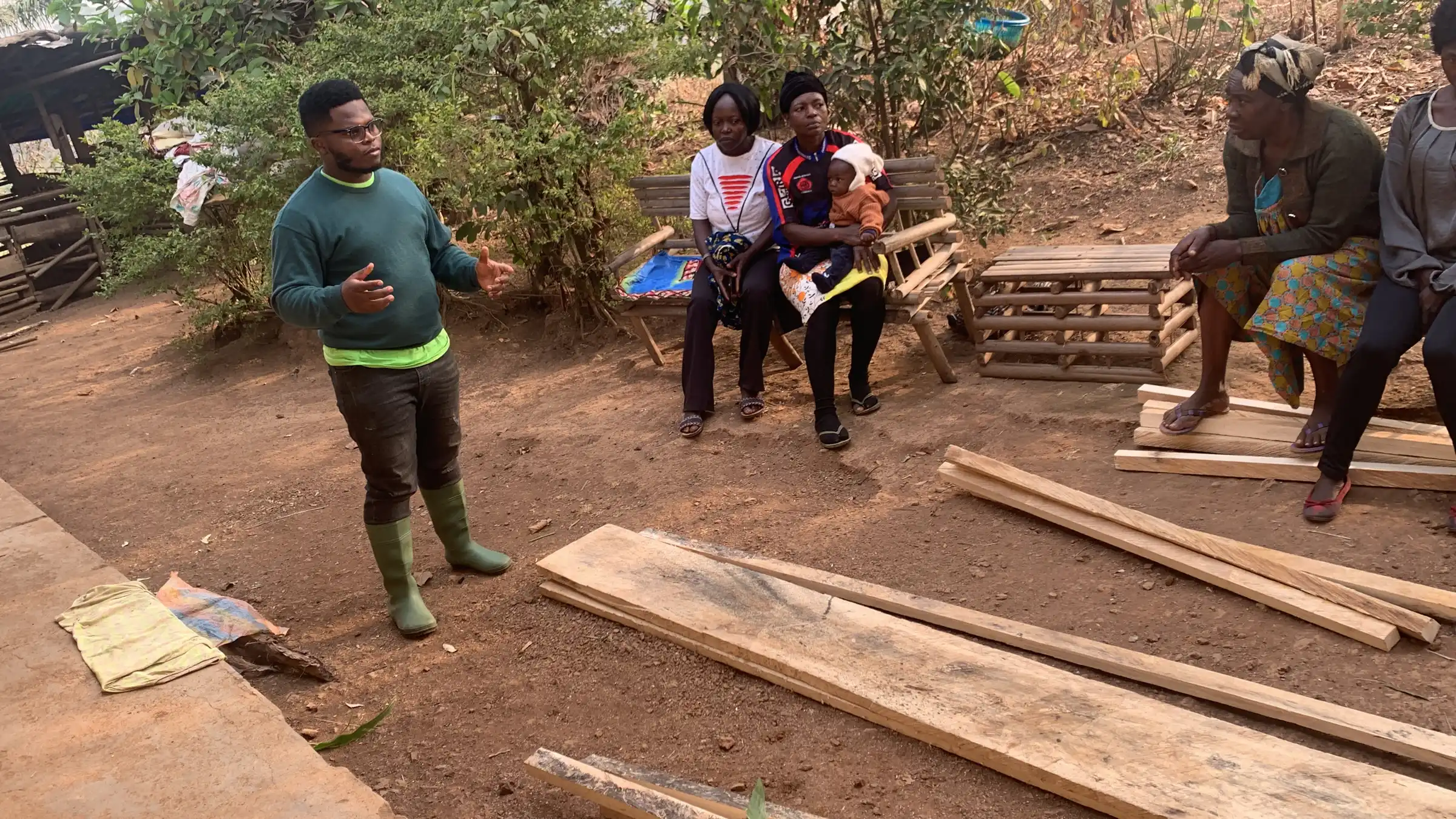 A trainer speaks to women beside stacked timber for raised beds
